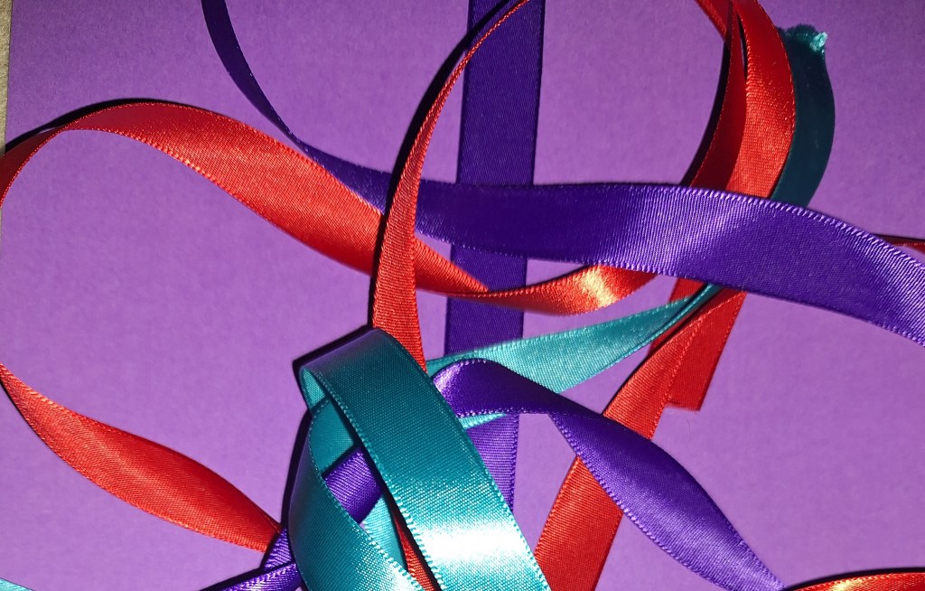 An assortment of colourful ribbons, including red, turquoise, and purple, laid over a purple background.
